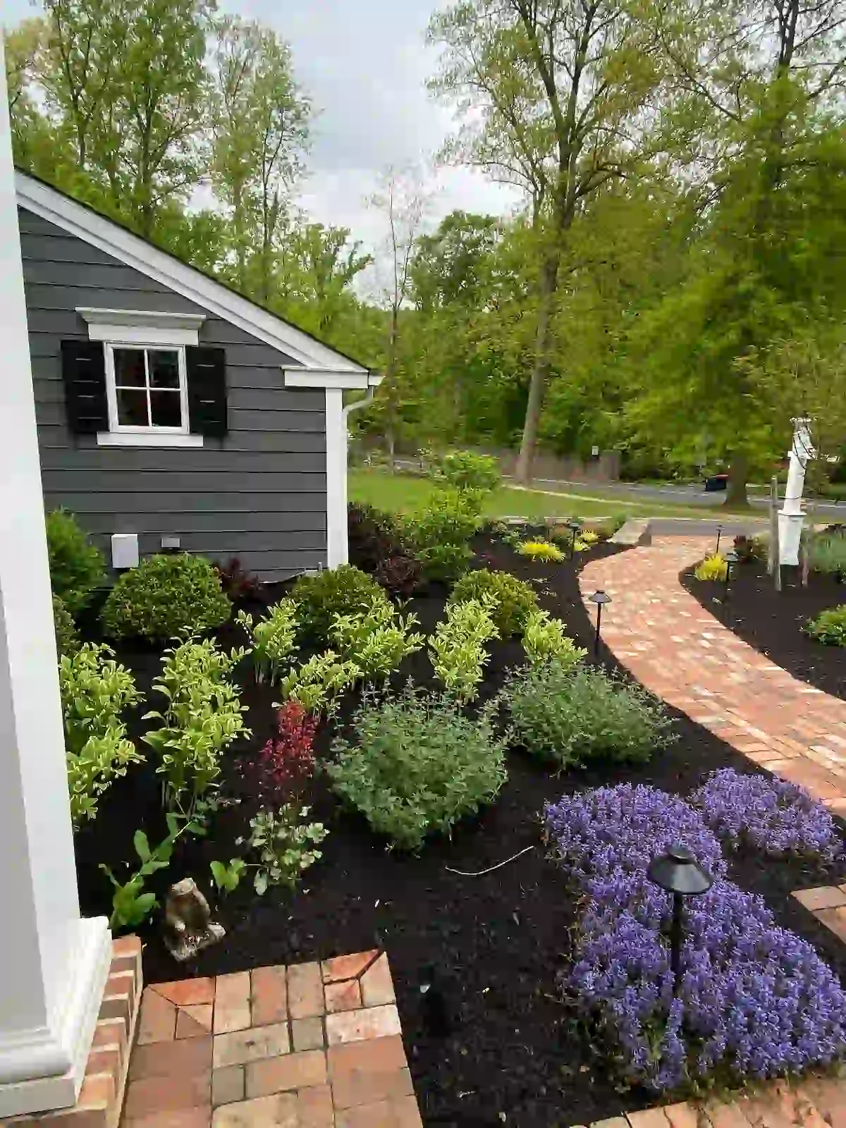 Garden bed installation with dark mulch and vibrant shrubs bordering a curved brick walkway.